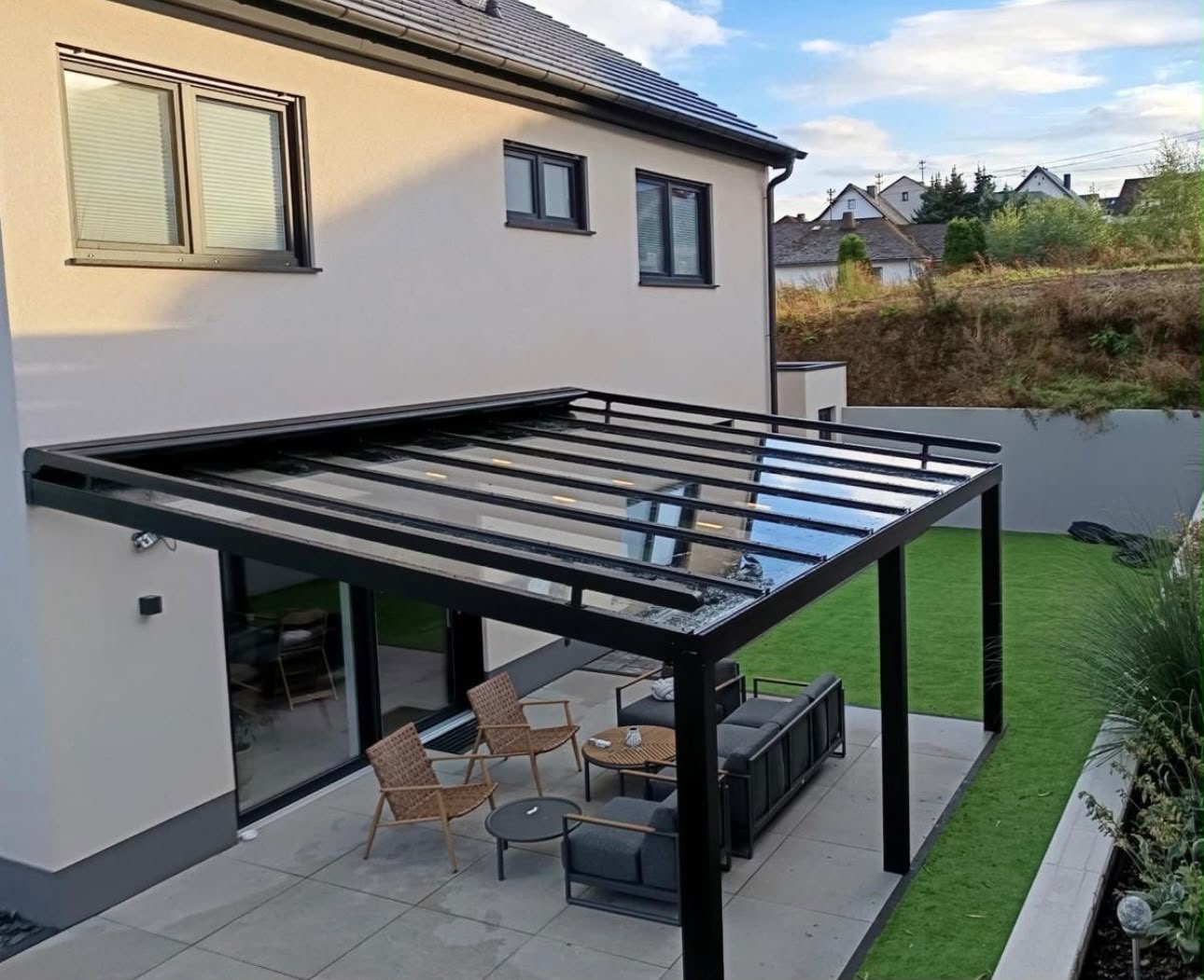 Freistehende Terrassenüberdachung mit Glasdach und Sitzgruppe im Garten eines Einfamilienhauses