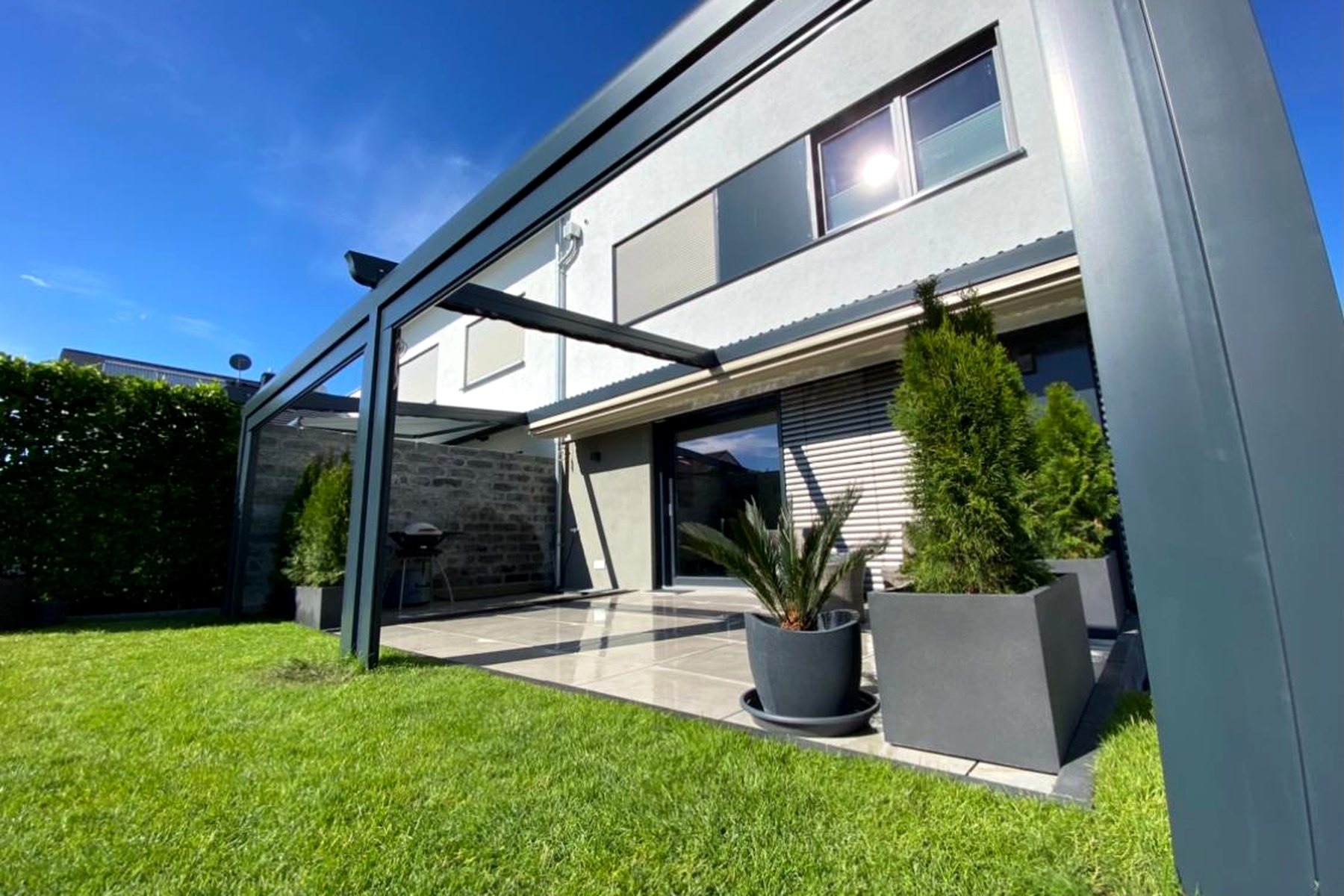 Freistehende Pergola in hellem Farbton neben einem modernen Wohnhaus mit Rasenfläche