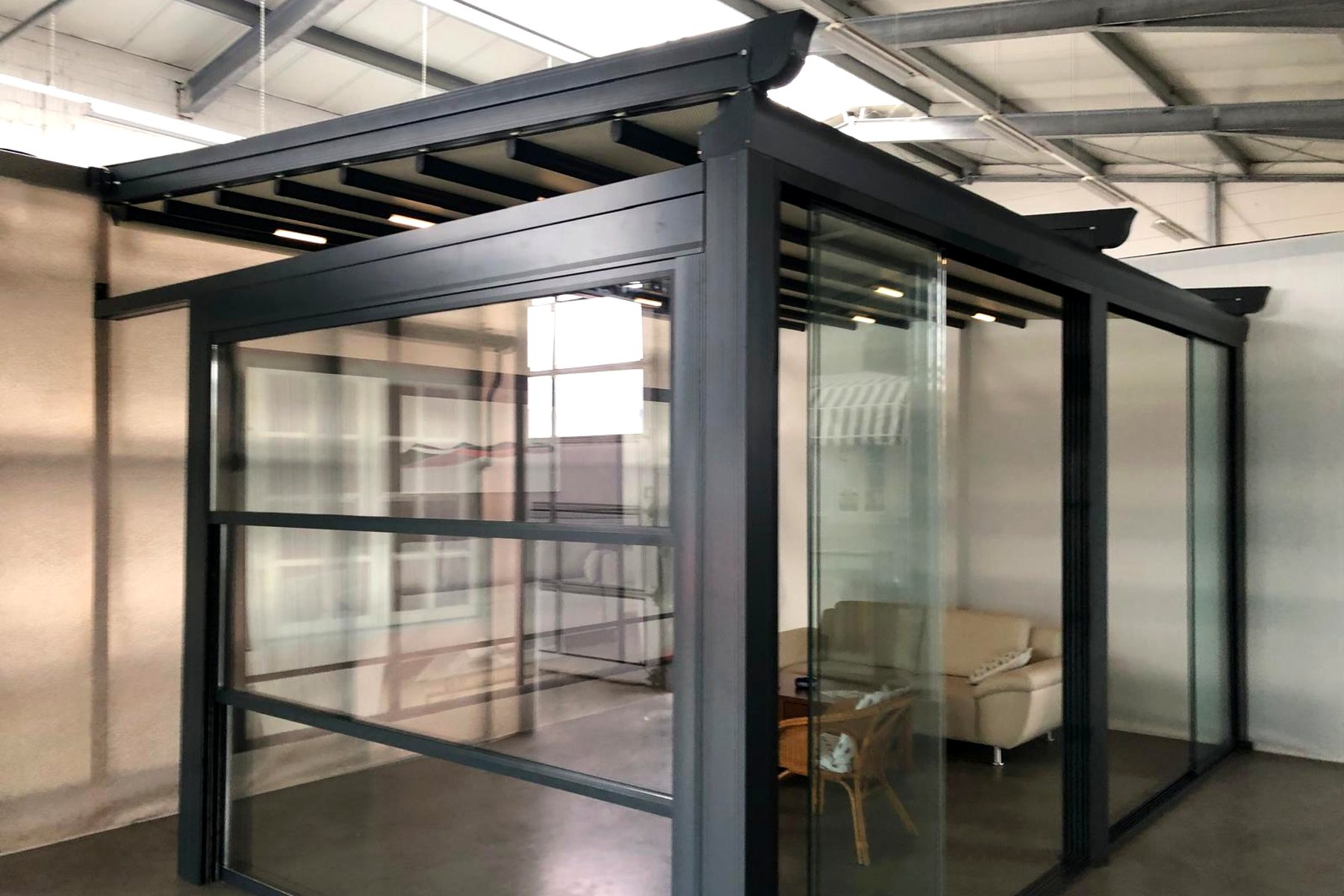 Frontansicht einer anthrazitfarbenen Pergola mit Glasdach an einem Wohnhaus