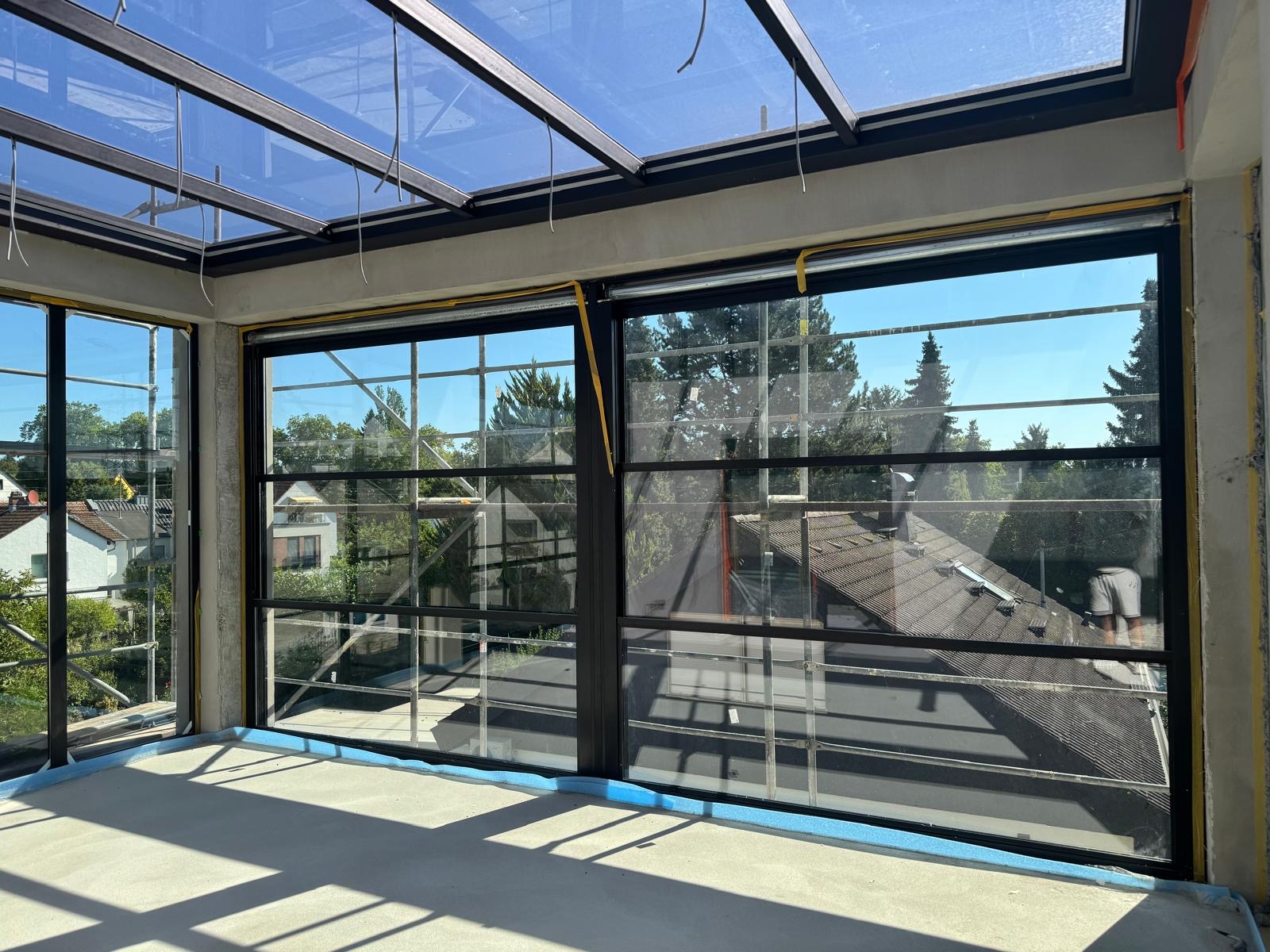 Blick von innen durch ein Glasdach mit schlanken Aluminiumsprossen in den Garten