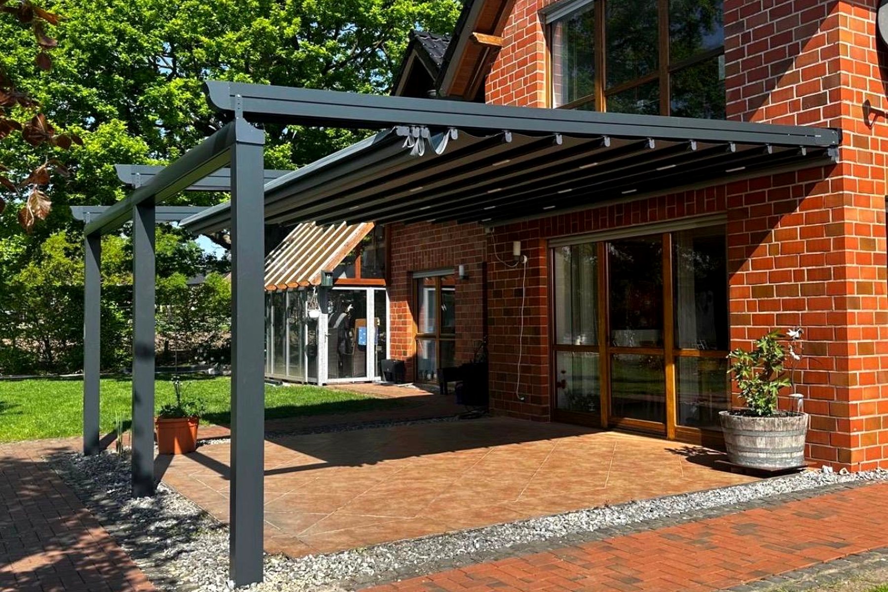 Pergola-Überdachung an einer Klinkerfassade mit gepflasterter Terrasse