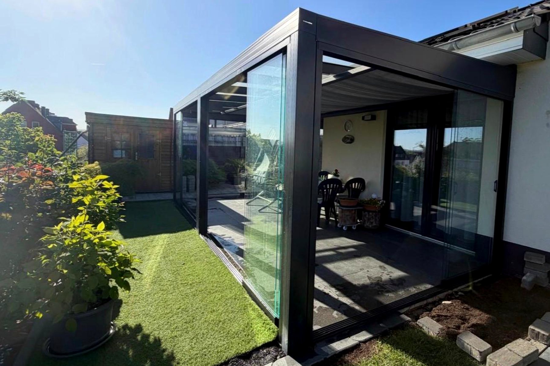 Verglaster Terrassenanbau mit Glasdach an einem Wohnhaus mit Rasenfläche