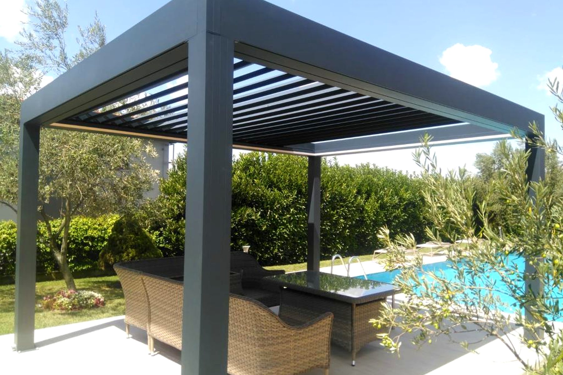 Lamellendach mit anthrazitfarbenen Profilen über einer Terrasse mit Blick auf einen Pool