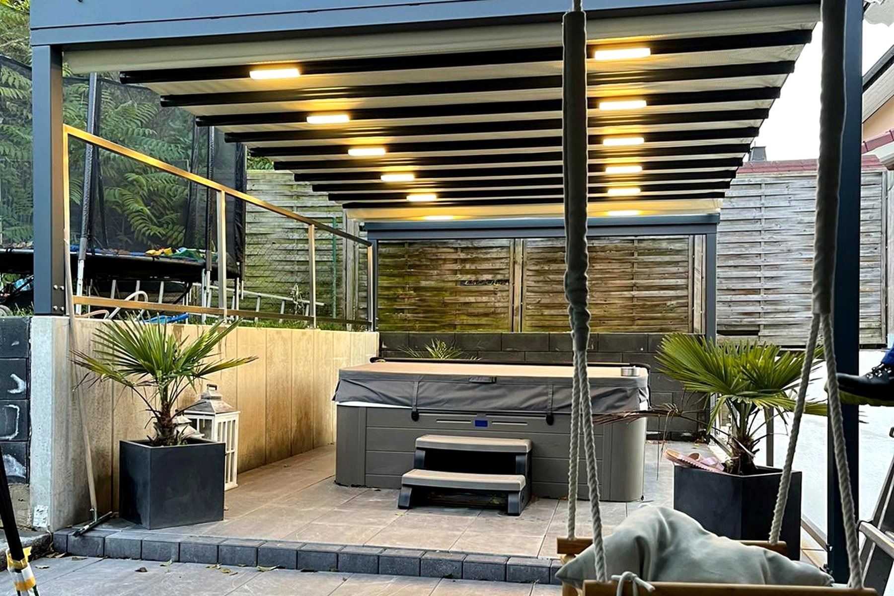 Pergola-Überdachung über einer Terrasse mit Lounge-Möbeln und Pflanzkübeln bei Tag