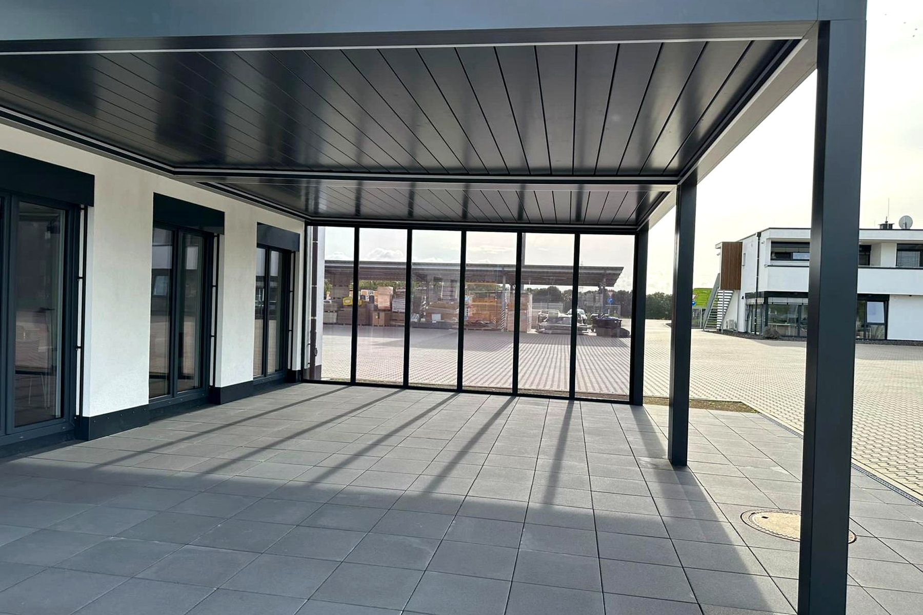 Anthrazitfarbenes Lamellendach über einer großen Terrasse an einem weißen Haus